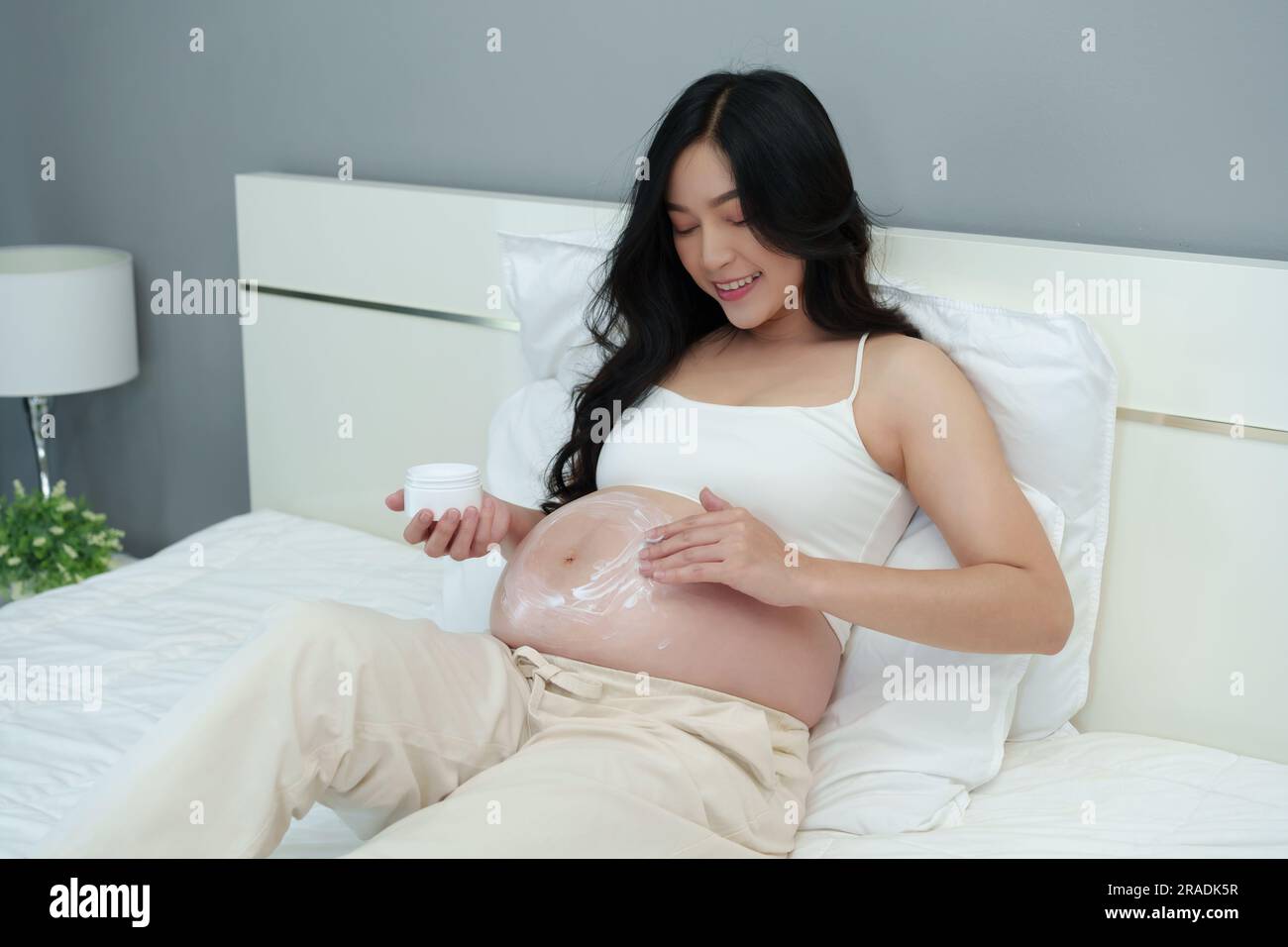 femme enceinte à la course appliquez de la crème sur son ventre pour hydrater la peau de beauté sur un lit Banque D'Images