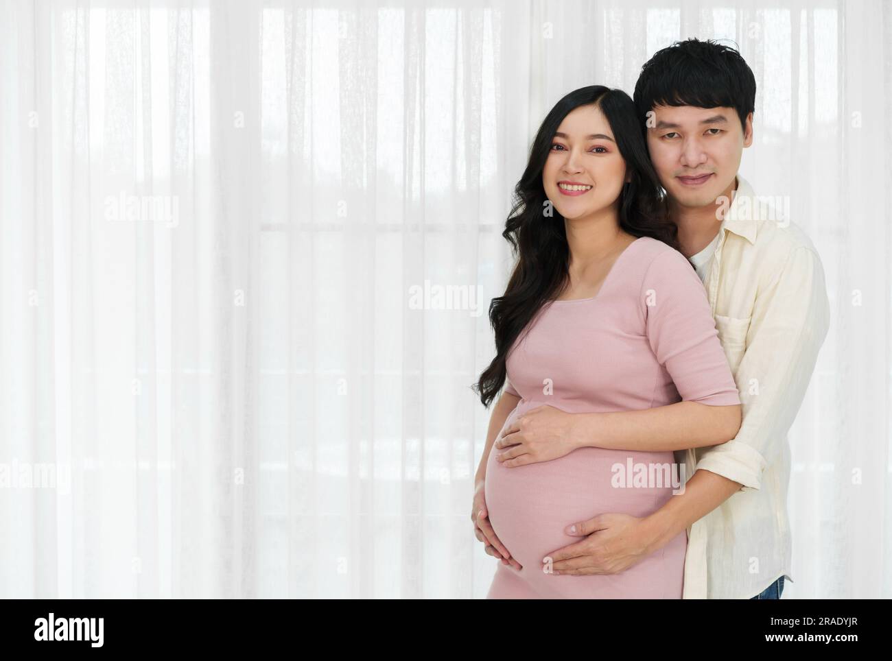 le couple marié attend bébé. l'homme embrasse sa femme enceinte sur un fond de fenêtre Banque D'Images