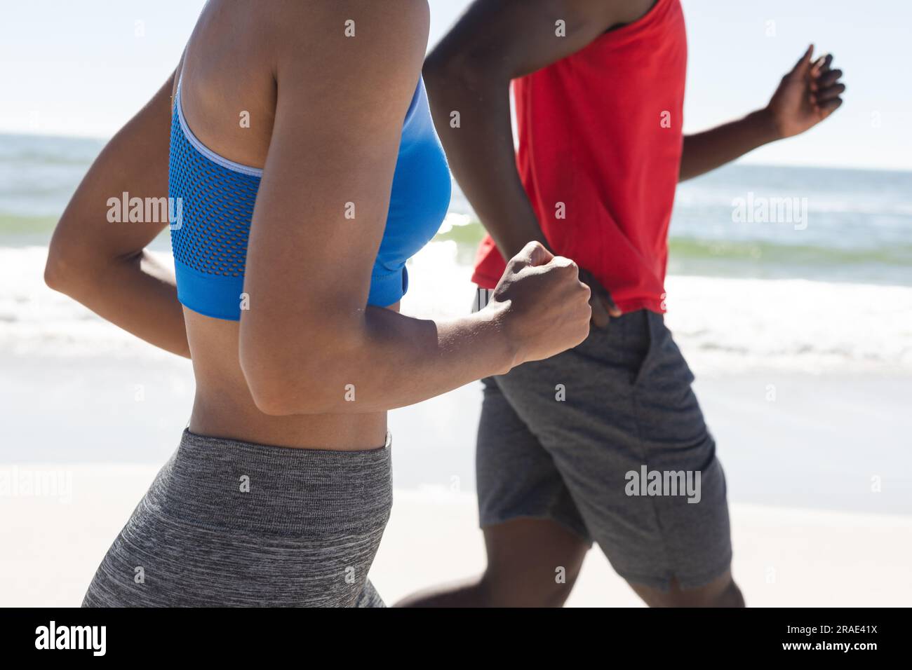 Section médiane de couple afro-américain en forme s'exerçant, courir sur la plage ensoleillée Banque D'Images