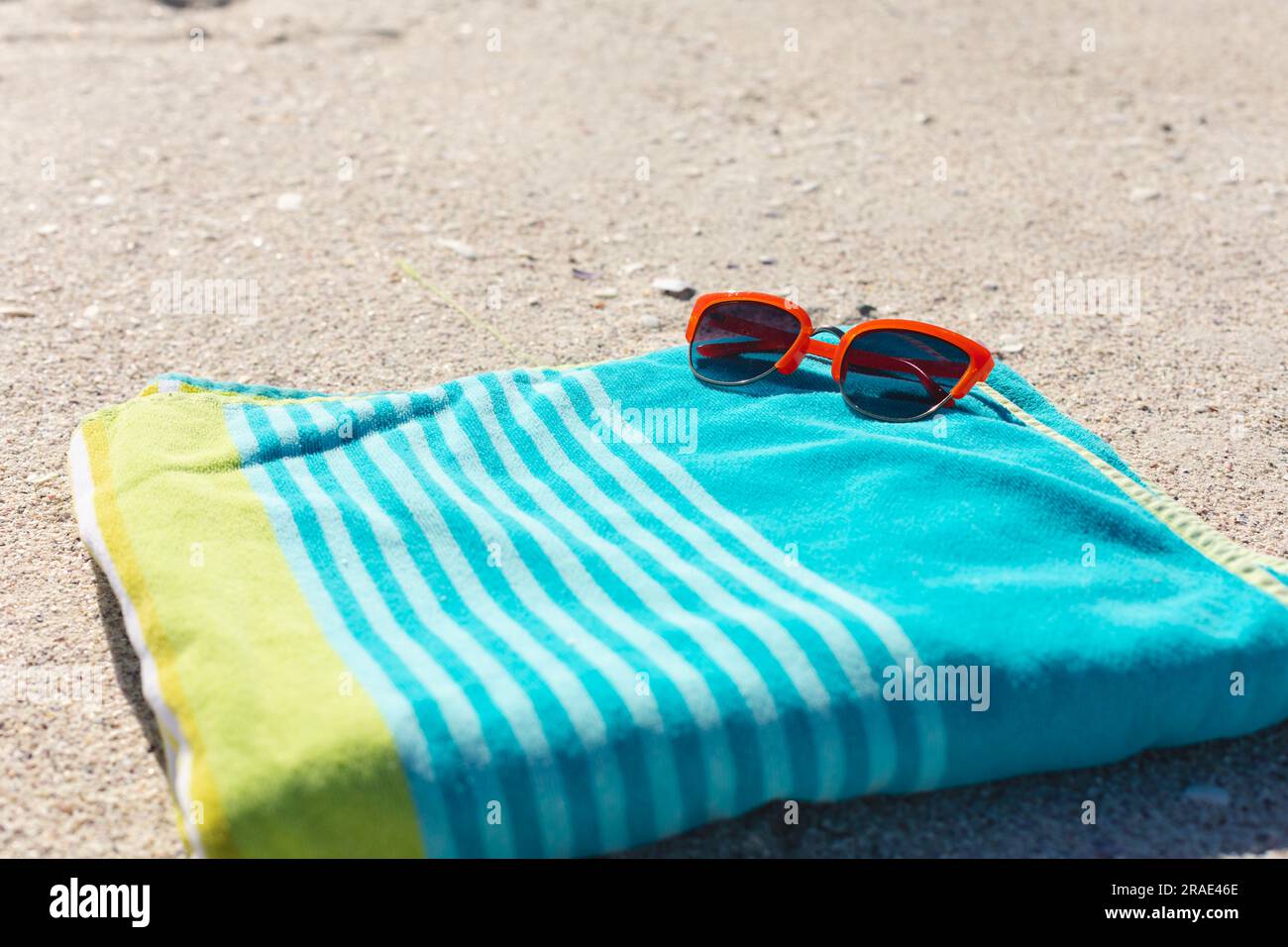 Lunettes de soleil rouges sur serviette rayée verte et bleue sur plage de sable ensoleillée, espace copie Banque D'Images