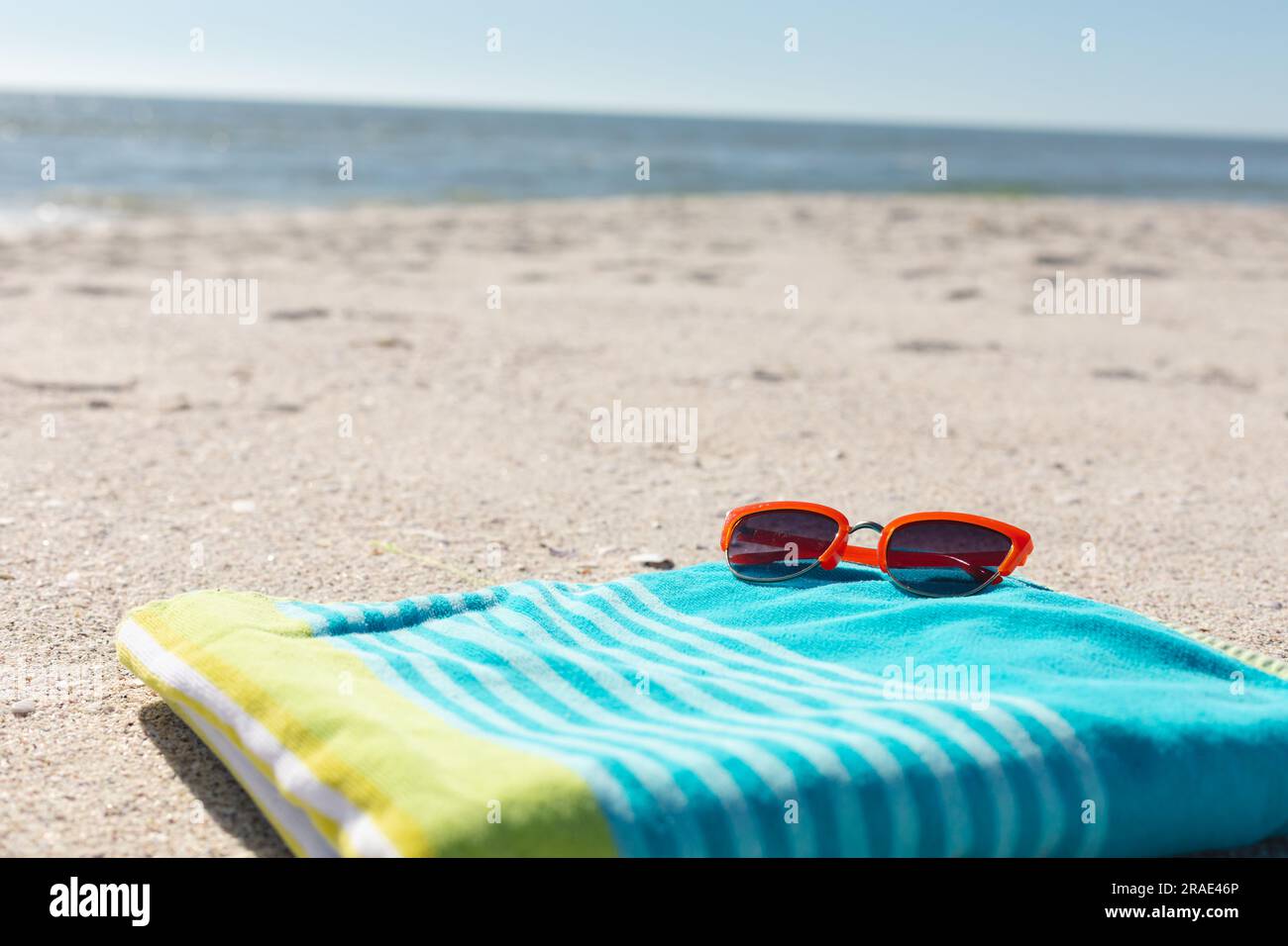 Lunettes de soleil rouges sur serviette rayée verte et bleue sur plage de sable ensoleillée au bord de la mer, espace copie Banque D'Images