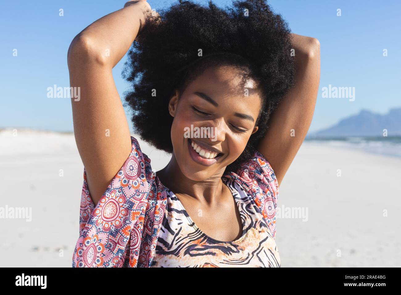 Heureuse femme afro-américaine sur la plage ensoleillée, souriant avec les yeux fermés Banque D'Images