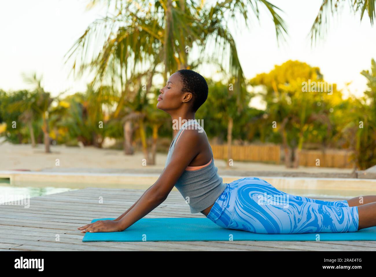 Heureuse femme afro-américaine pratiquant le yoga couché et étirant avec les yeux fermés sur la terrasse de la plage Banque D'Images