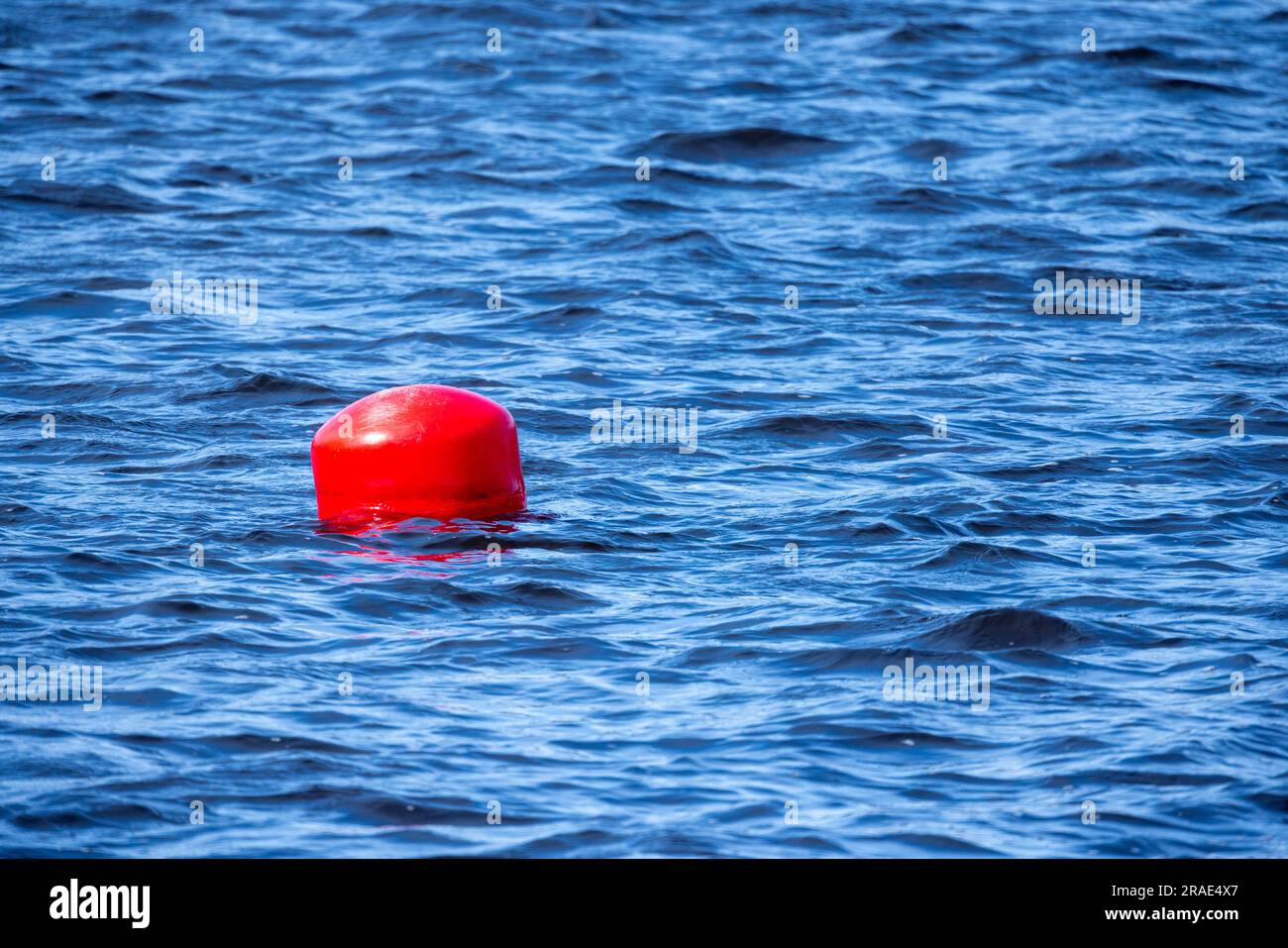 Bouée sphérique rouge flottant sur de l'eau de mer bleue par temps ensoleillé Banque D'Images