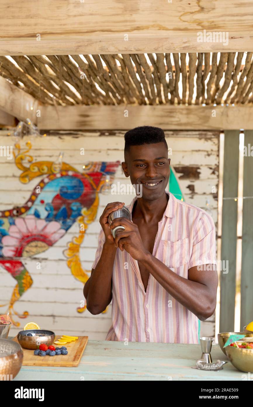 Joyeux barman afro-américain préparant un cocktail avec shaker derrière le comptoir au bar de la plage Banque D'Images