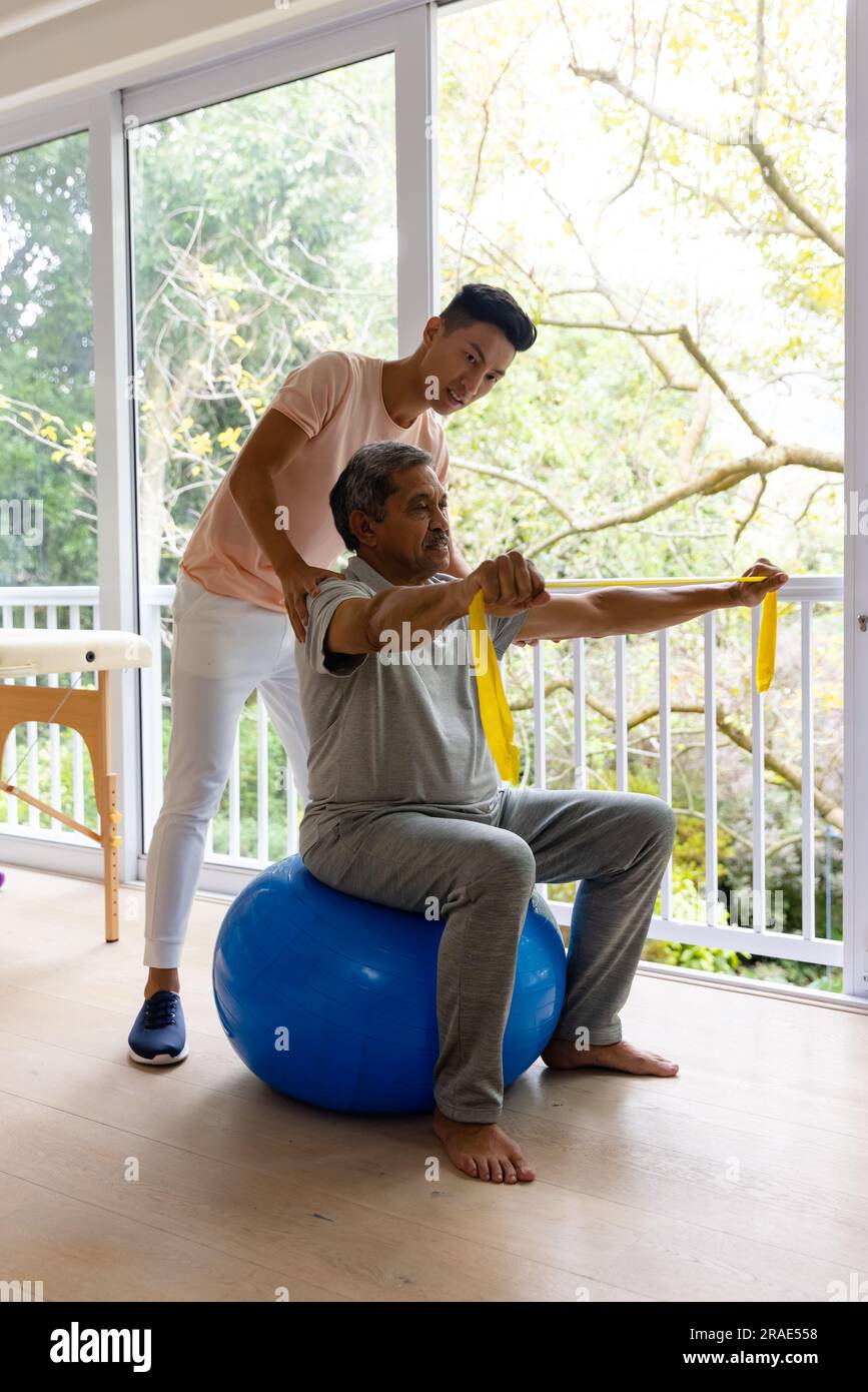 Physiothérapeute masculin diversifié conseillant et patient masculin senior utilisant la bande d'exercice Banque D'Images