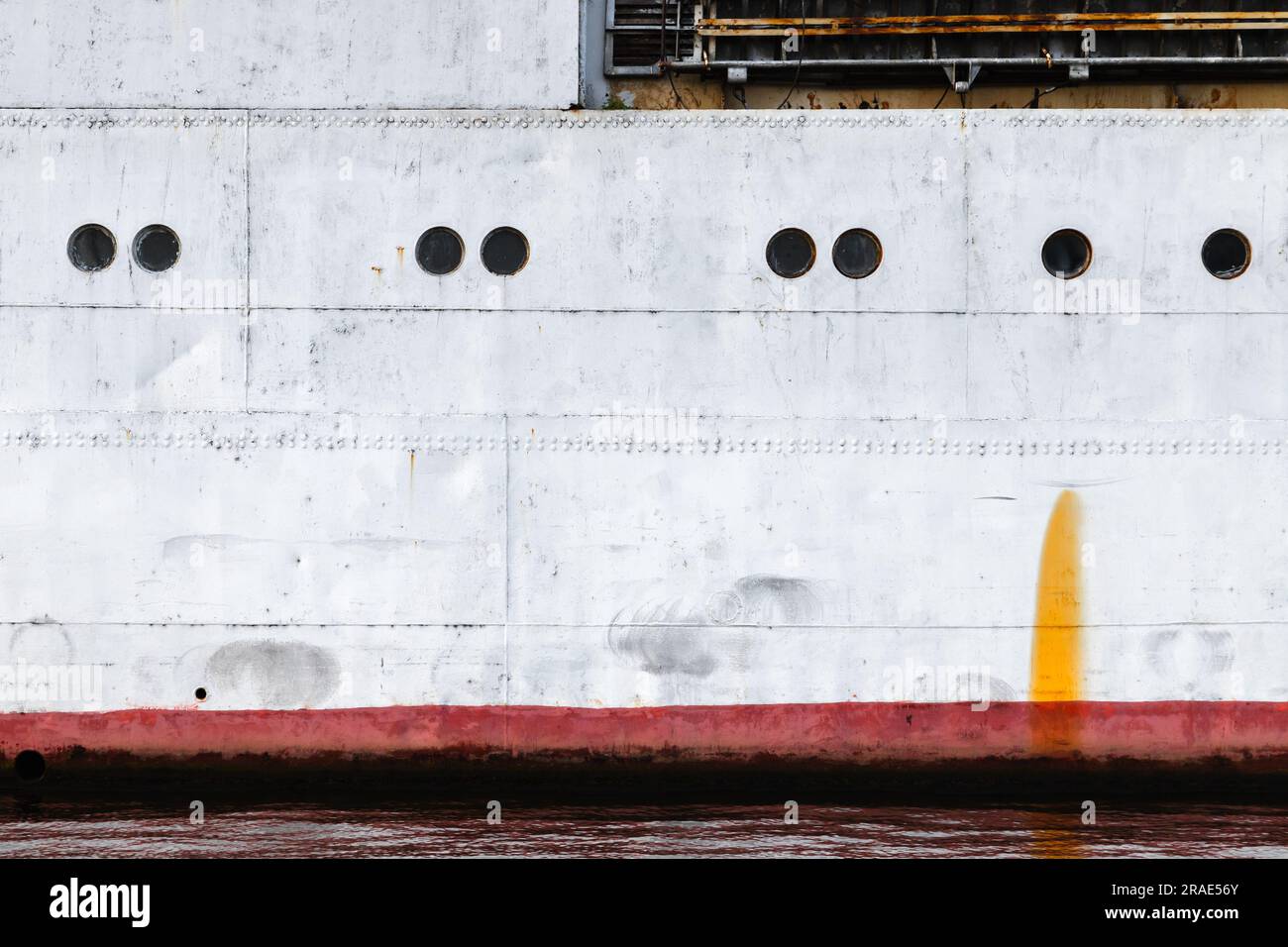 Coque de navire ancien avec ligne d'eau rouge et hublots, transport industriel arrière-plan texture photo Banque D'Images