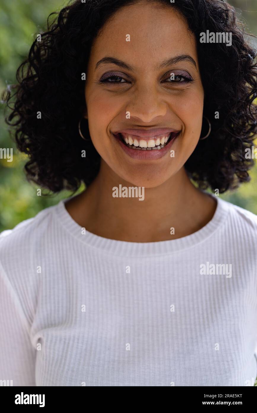 Portrait d'une femme biraciale souriante avec les cheveux noirs bouclés devant la cime des arbres Banque D'Images