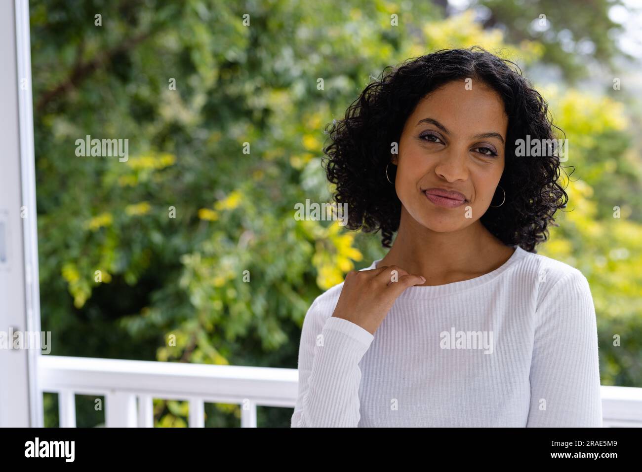 Portrait de souriante femme biraciale debout sur le balcon ensoleillé à la maison devant la cime des arbres Banque D'Images