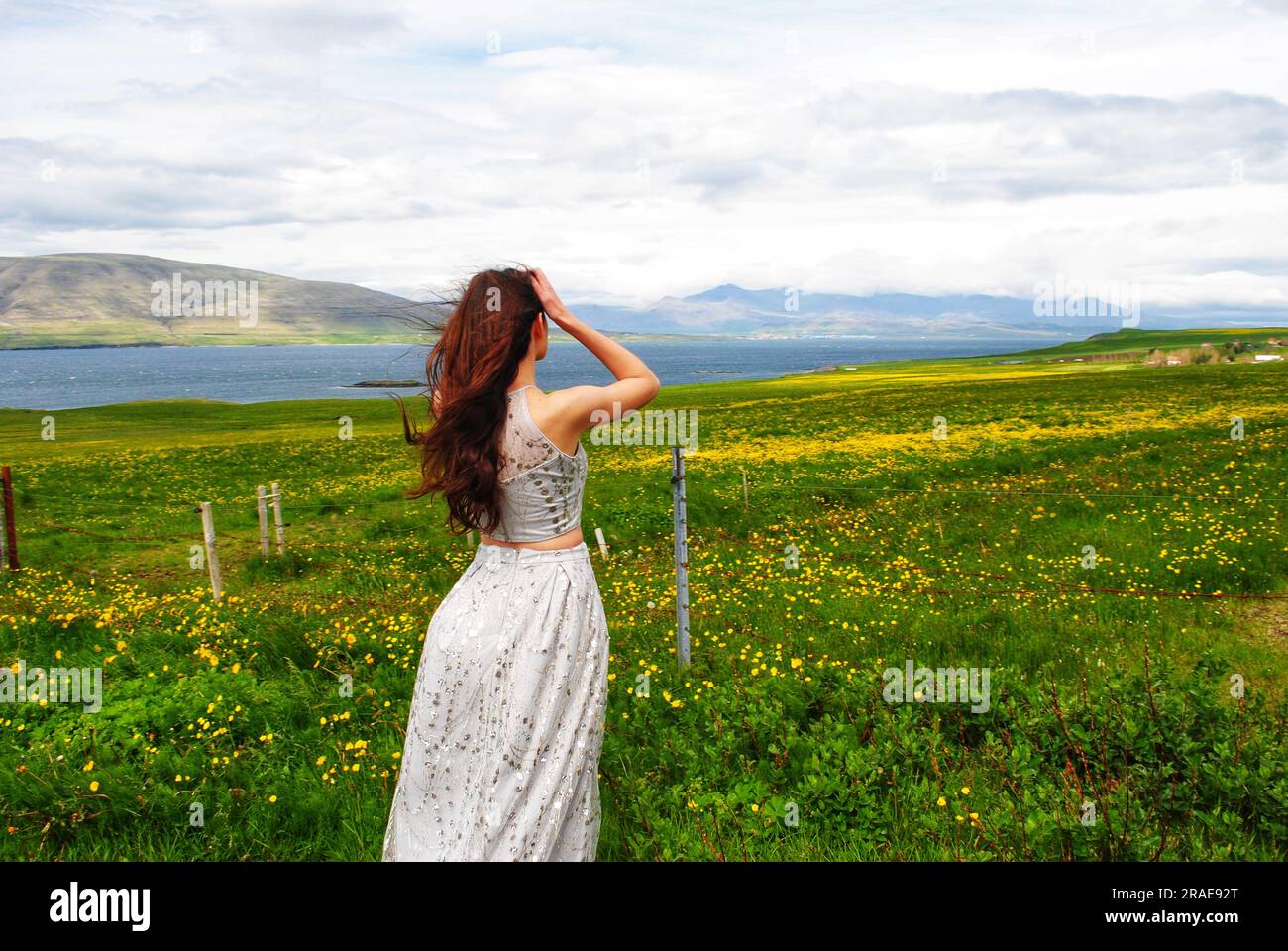 Une femme dans une robe argentée étincelante regarde les fleurs jaunes dans un champ près de Mossfellsbaer, en Islande. Banque D'Images