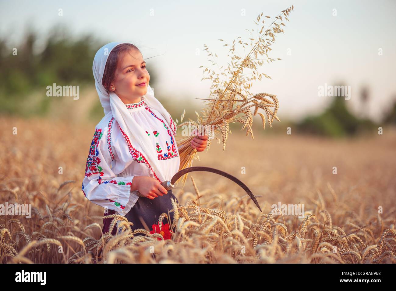 Femme paysanne bulgare petite fille en costume de folklore ethnique tenir des pailles de blé doré et la faucille dans le champ de récolte, la récolte et l'agriculture à Bulg Banque D'Images