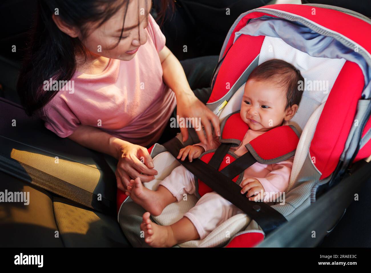 mère consolant son nouveau-né pleurant tout en mettant et attacher les ceintures de sécurité sur le siège de voiture Banque D'Images