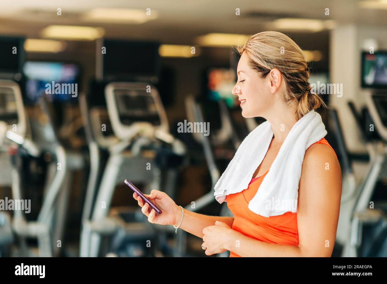 Femme heureuse et en bonne santé dans la salle de sport, tenant un smartphone Banque D'Images