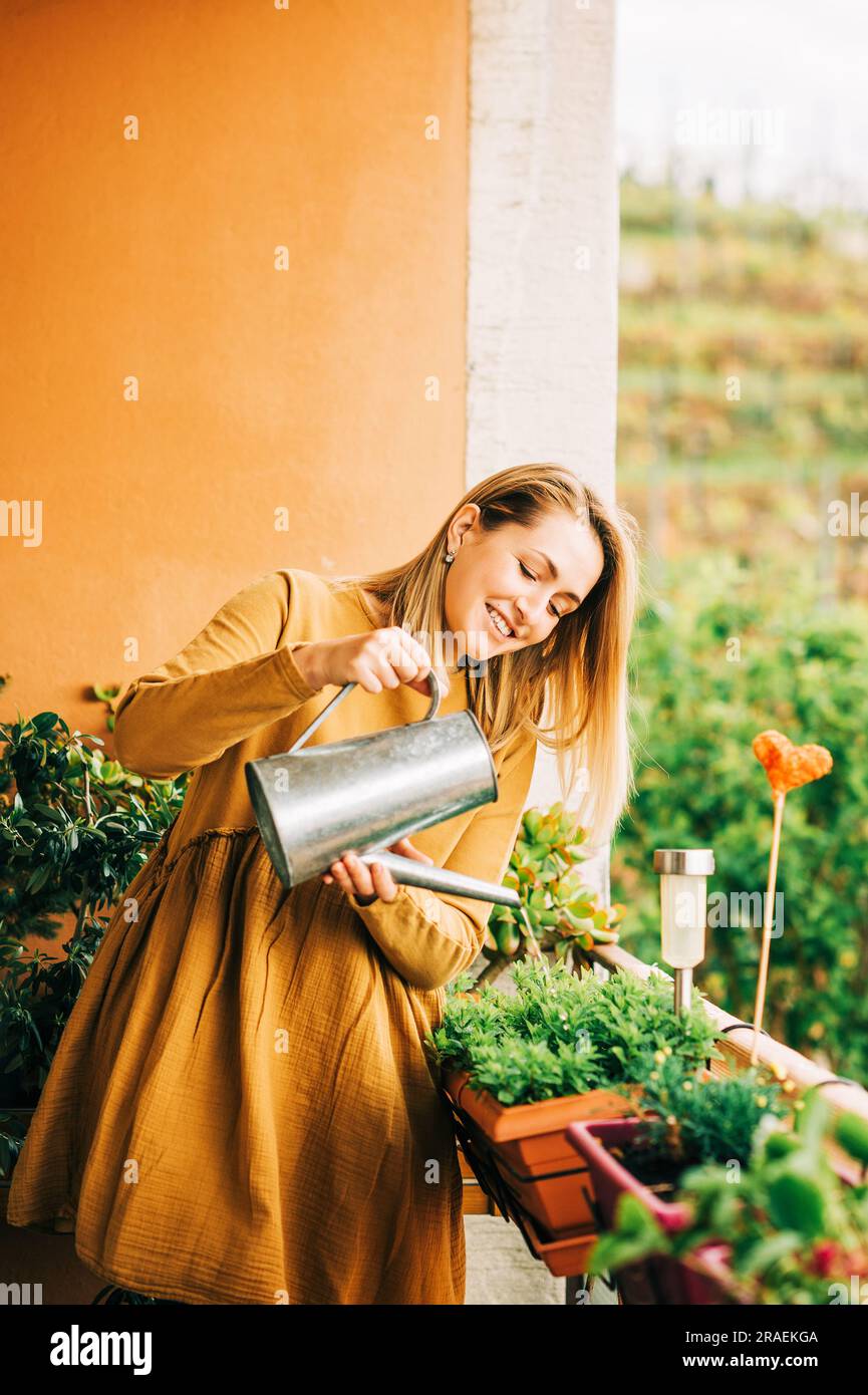 Portrait de la belle femme arroser des plantes vertes sur le balcon, portant une robe en coton brun Banque D'Images