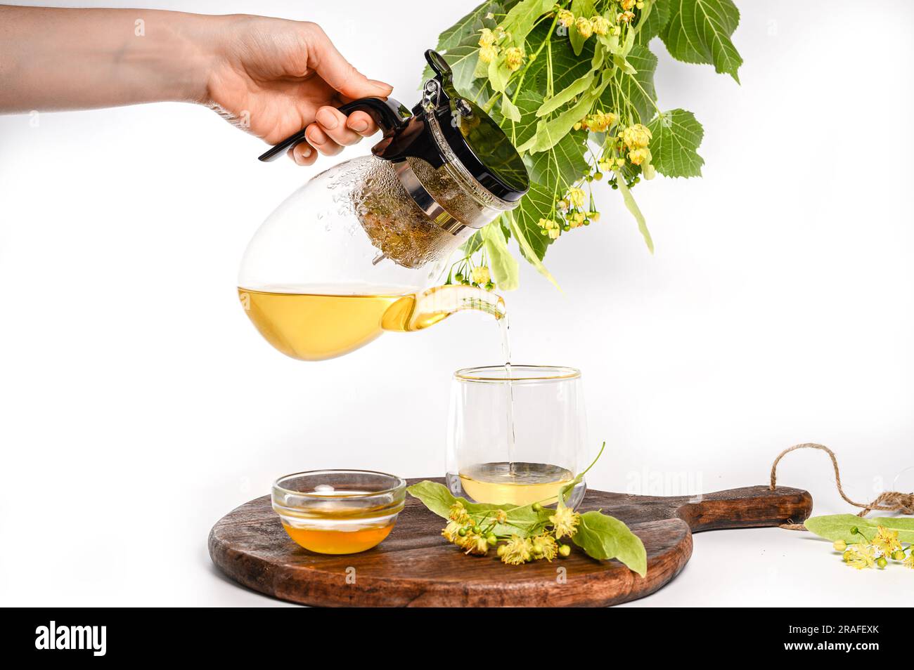 La main d'une femme verse du thé de linden fraîchement préparé dans une tasse transparente. Banque D'Images