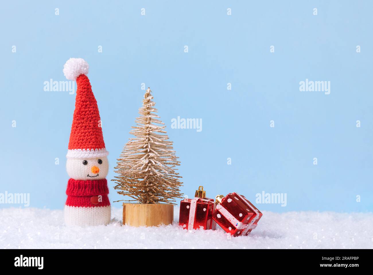 Bonhomme de neige tricoté dans un chapeau de Noël rouge et un chandail avec deux cadeaux rouges sous le jouet arbre de Noël . Carte de vœux de Noël et du nouvel an 2024. Banque D'Images