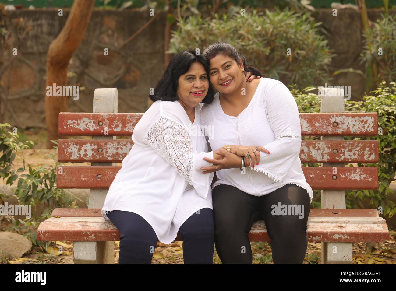 Heureuse mère indienne et fille en robe blanche ayant de beaux moments assis sur le banc dans le parc de la ville. Mère aimante et fille adorable. Banque D'Images