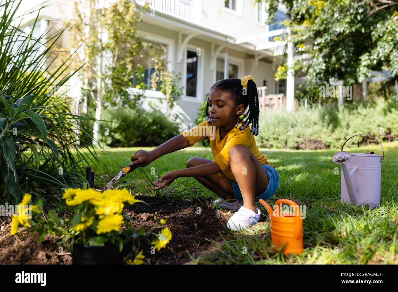 Fille afro-américaine creusant la terre avec l'outil sur la terre herbeuse dans la cour à l'extérieur de la maison Banque D'Images