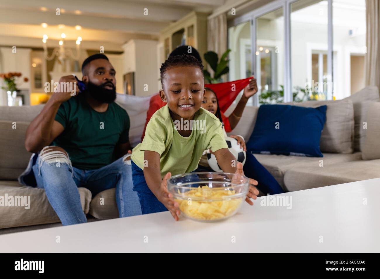 Heureux parents afro-américains avec fils et fille avec drapeau regardant le sport à la télévision à la maison Banque D'Images