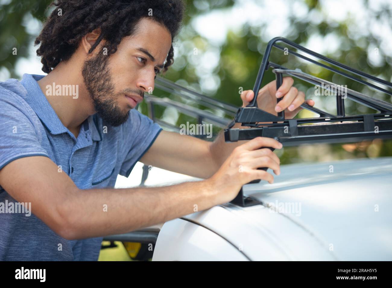 un jeune homme sérieux fixe la galerie de toit sur la voiture Banque D'Images