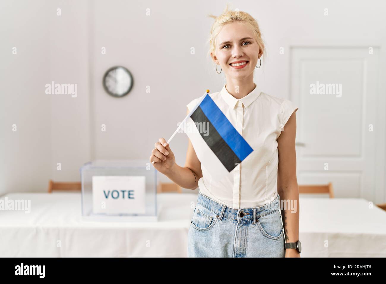 Jeune femme blonde portant le drapeau estonien souriant au collège électoral Banque D'Images