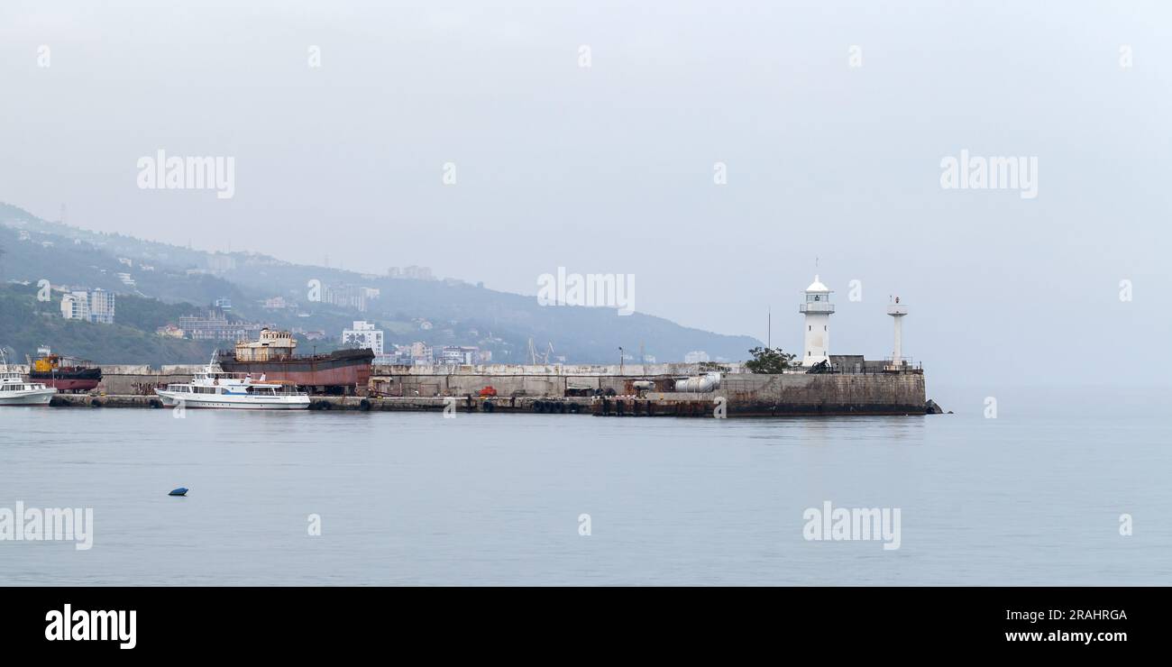 Vue panoramique sur le port de Yalta. La tour blanche du phare est sur un brise-lames le jour d'un ciel nuageux Banque D'Images