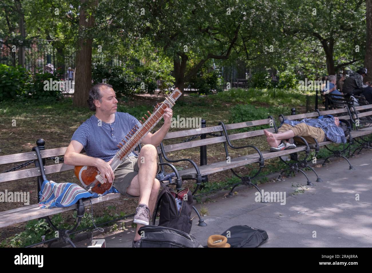 Une scène de rue de New York avec un joueur de sitar non hindou près d'un homme endormi sans chaussures. Dans Washington Square Park à Greenwich Village, New York. Banque D'Images