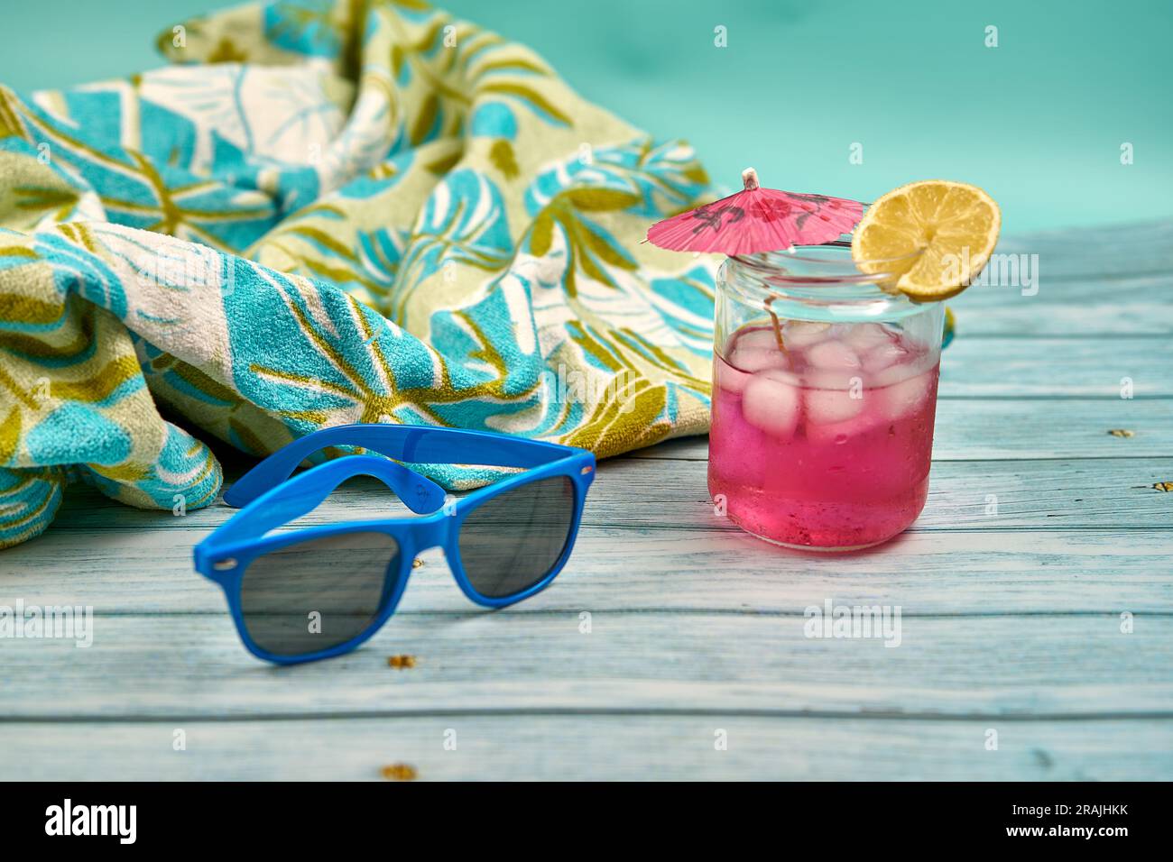 Boisson rafraîchissante d'été avec beaucoup de glace un parapluie et une tranche de citron, lunettes de soleil bleues et serviette de plage à motifs tropicaux sur une table en bois et un Banque D'Images