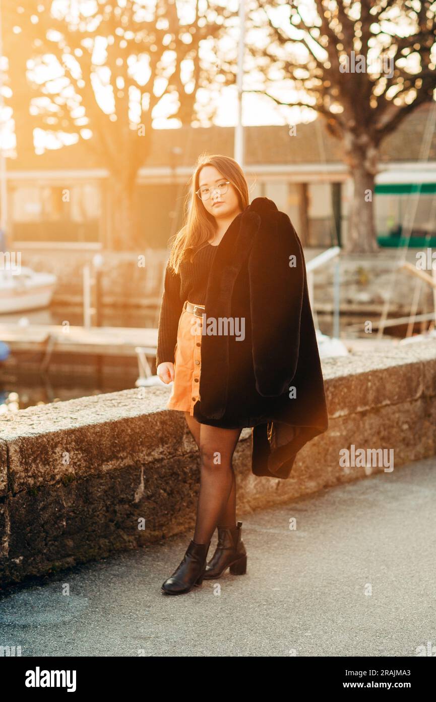 Portrait extérieur d'un modèle asiatique de taille plus, tenant un manteau noir en fausse fourrure, posant près du lac Banque D'Images