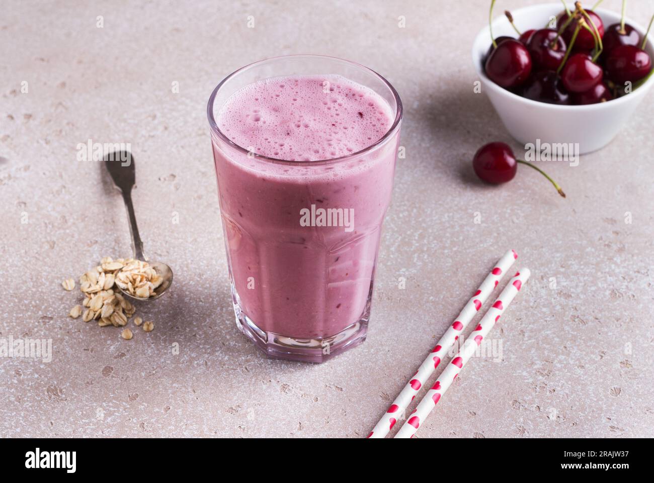 Milk-Shake avec cerises, yaourt et flocons d'avoine, pailles à boire, bol avec cerises fraîches sur fond beige texturé. Banque D'Images
