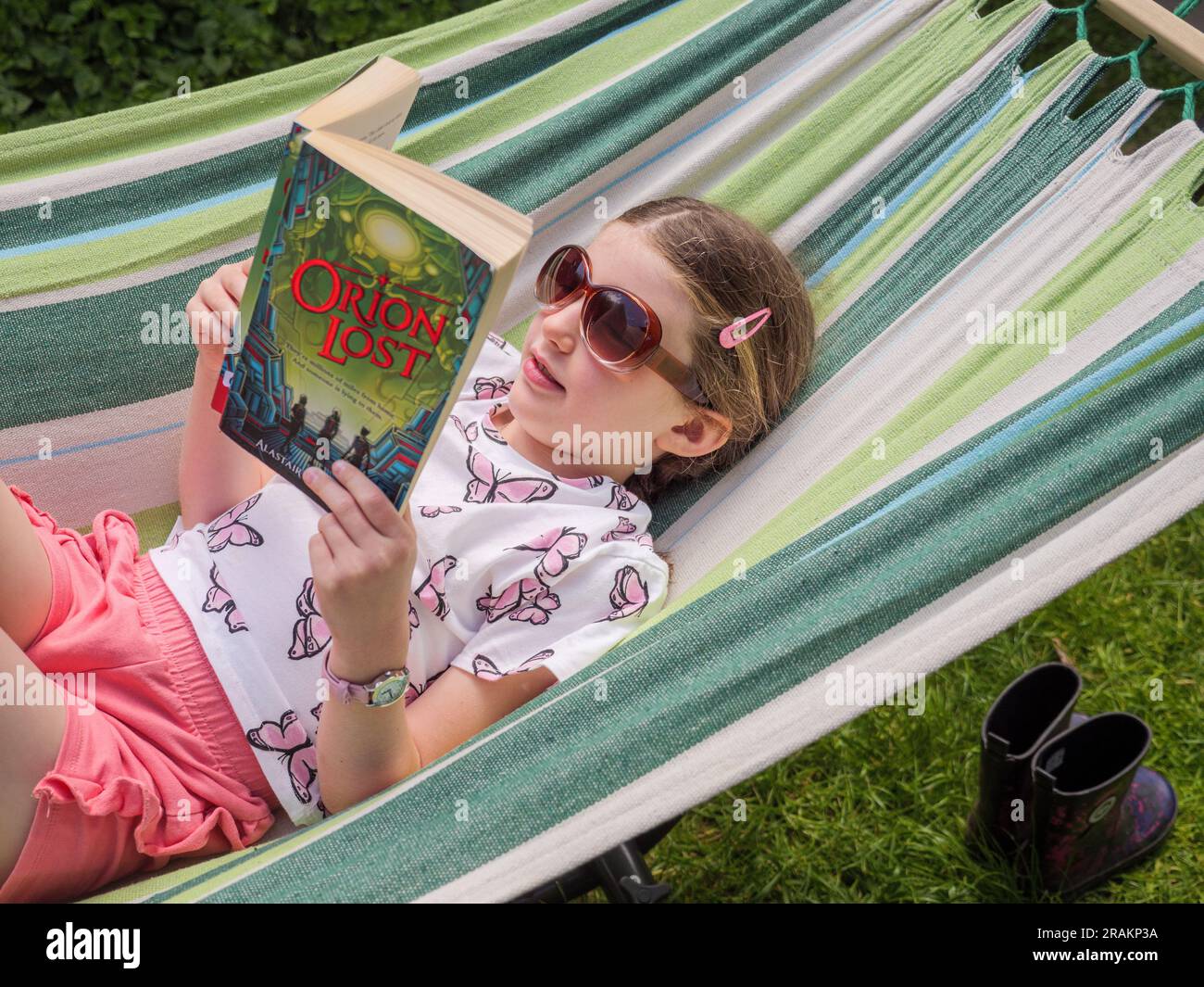 Jeune fille lisant un roman de livre de fiction à l'extérieur sur un hamac de jardin Banque D'Images