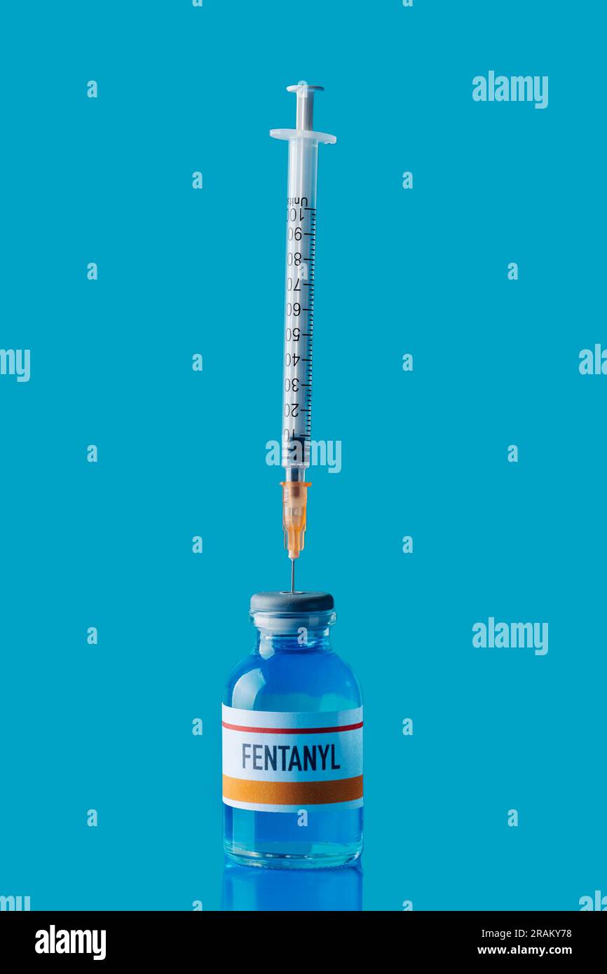 un flacon simulé de fentanyl avec une seringue dans son bouchon en caoutchouc sur une surface bleue sur fond bleu Banque D'Images
