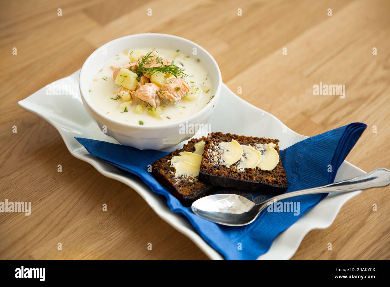 Un bol de soupe finlandaise Lohikeitto servi sur une table en bois avec un morceau de pain de seigle suédois. Bouillon crémeux, pommes de terre tendres et saumon rose feuilleté Banque D'Images