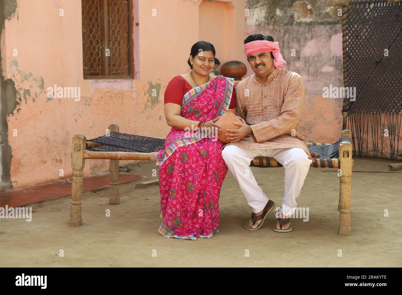 Femmes indiennes rurales heureuses à Saree assis avec son mari tenant la banque de Piggy. Famille aspirative montrant son amour envers leur argent économisé. Banque D'Images