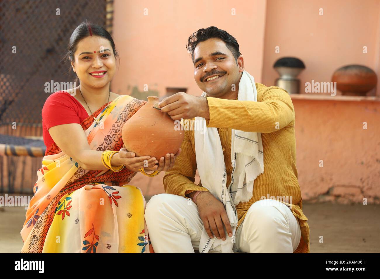 Femmes indiennes rurales heureuses à Saree assis avec son mari tenant Piggy Bank. Famille montrant son amour envers leur argent économisé. Insertion de pièces de monnaie. Banque D'Images