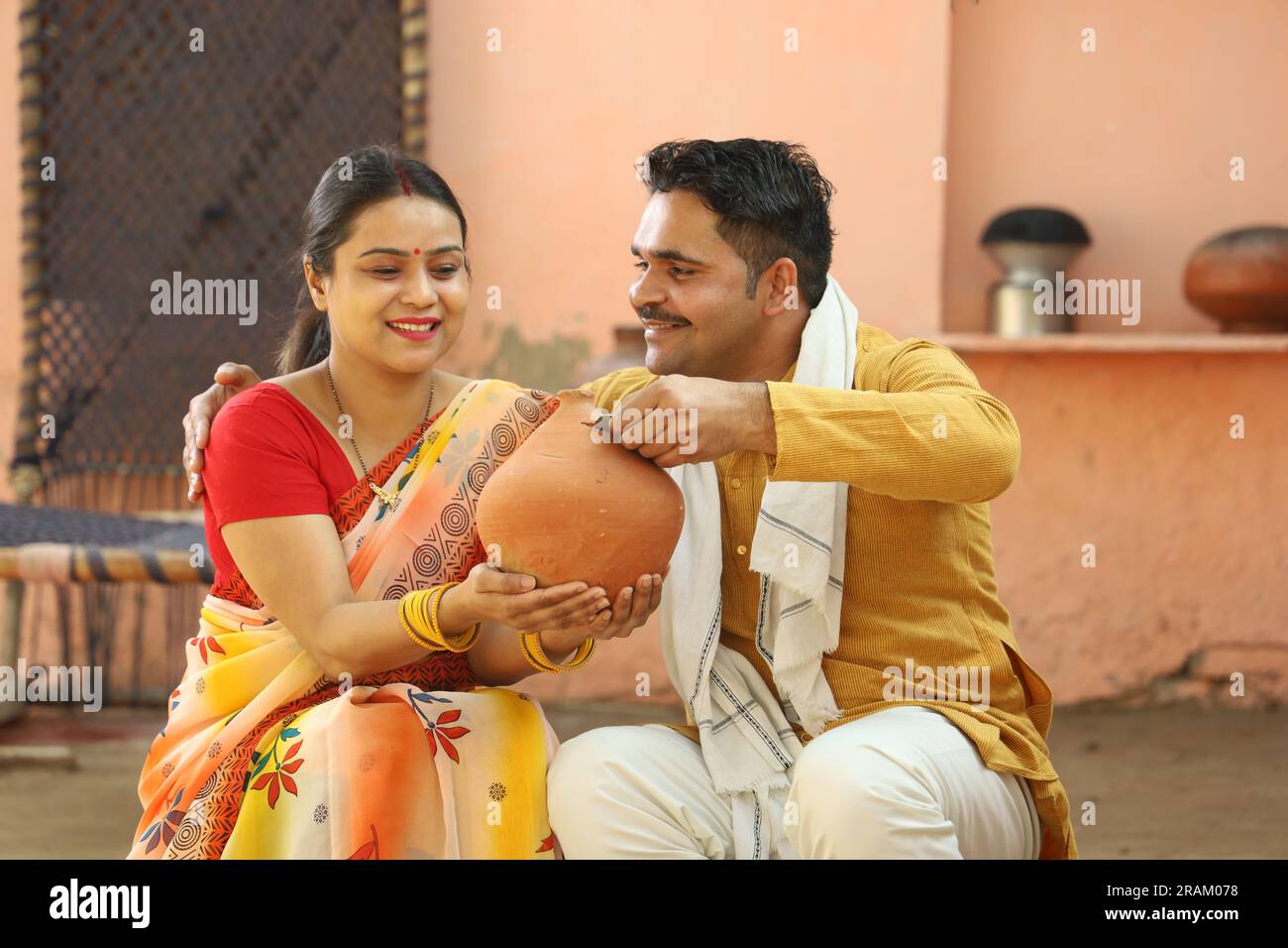 Femmes indiennes rurales heureuses à Saree assis avec son mari tenant Piggy Bank. Famille montrant son amour envers leur argent économisé. Insertion de pièces de monnaie. Banque D'Images