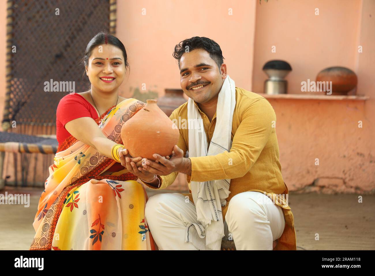 Femmes indiennes rurales heureuses à Saree assis avec son mari tenant Piggy Bank. Famille montrant son amour envers leur argent économisé. Insertion de pièces de monnaie. Banque D'Images