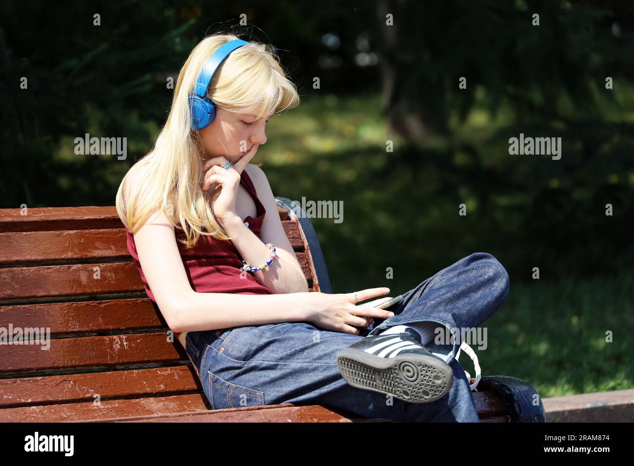 Fille blonde dans les écouteurs assis sur la rue de la ville avec smartphone dans les mains Banque D'Images
