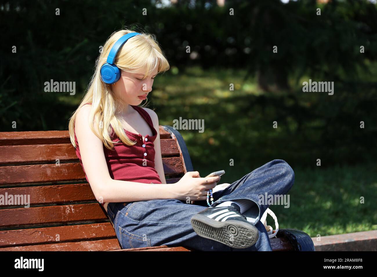 Fille blonde dans les écouteurs assis sur la rue de la ville avec smartphone dans les mains Banque D'Images