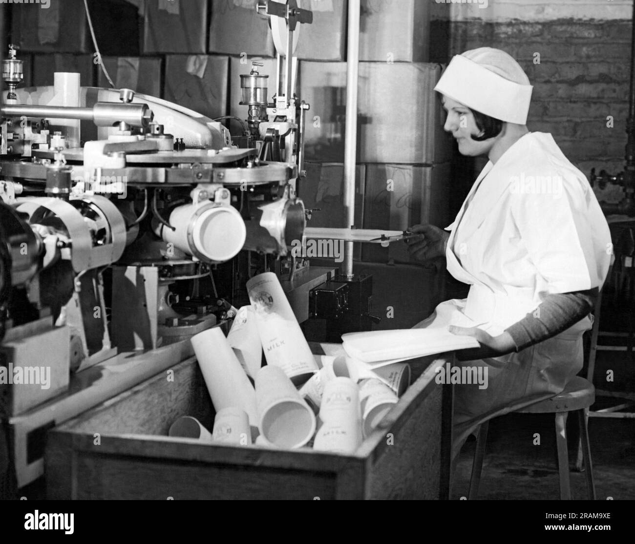 New York, New York: c. 1928 Sheffield Dairy Farms les travailleurs qui utilisent les nouveaux récipients en papier Sealcone pour emballer le lait, remplaçant la bouteille en verre. Ils sont plus légers, ils ne se cassent pas et sont deux fois plus efficaces en raison de leur forme conique. Ici, les conteneurs sont fabriqués à partir de feuilles de papier fibre d'épinette par la main droite du travailleur et qui sont introduits dans la machine toutes les trois secondes. Banque D'Images
