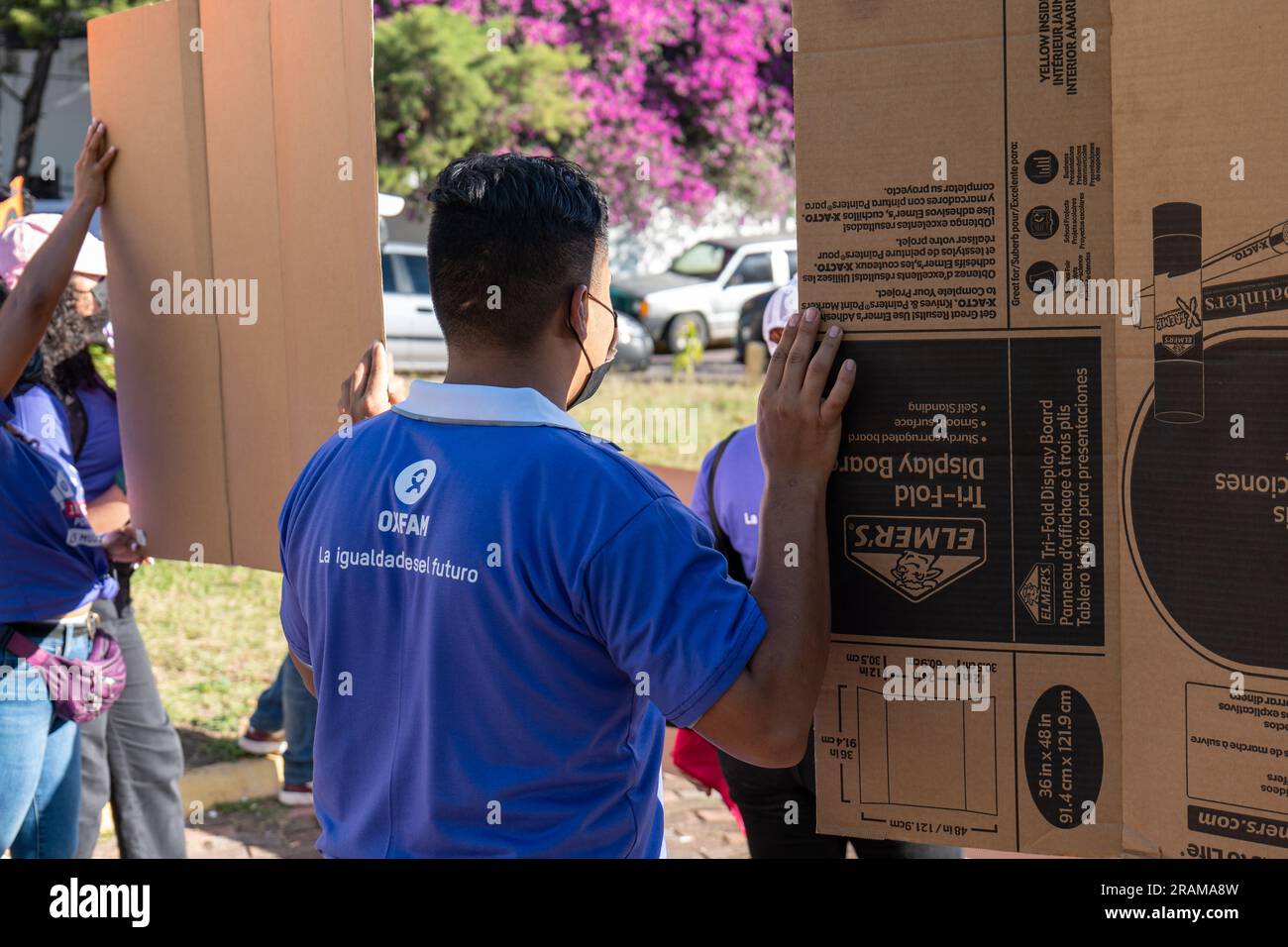 Tegucigalpa, Francisco Morazan, Honduras - 11 décembre 2022 : un jeune homme brun avec une chemise violette avec le logo Oxfam à l'arrière tient des panneaux en carton à A. Banque D'Images