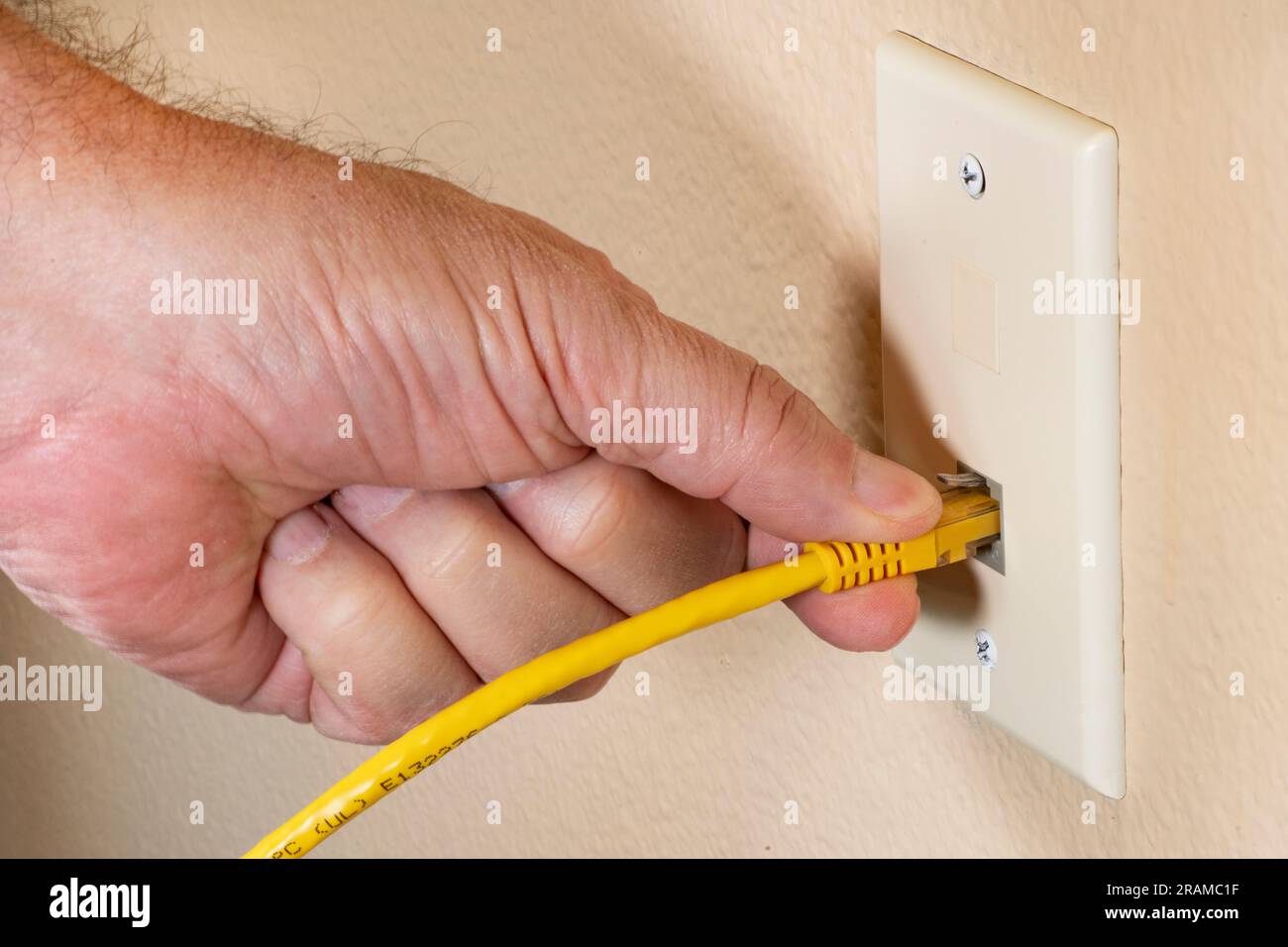 Main d'homme branchant le câble ethernet jaune RJ45 dans la prise réseau domestique Banque D'Images