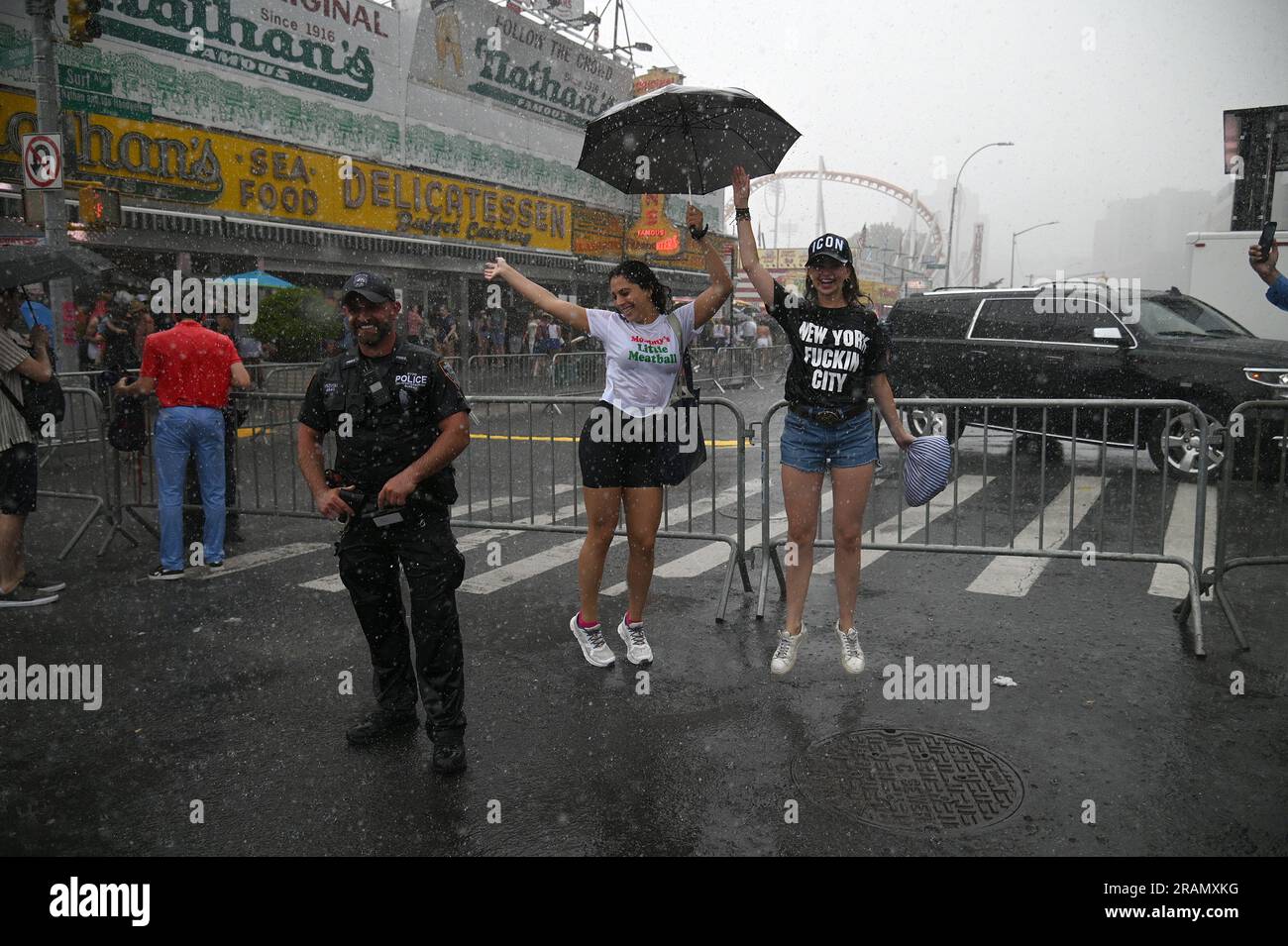 New York, États-Unis. 04th juillet 2023. Deux femmes dansent sous la pluie le long de Surf Avenue, à côté d'un officier du NYPD à Coney Island, dans le quartier de Brooklyn, New York, 4 juillet 2023. L'orage a entraîné le report d'une partie du célèbre concours de nourriture pour chiens chauds du 4 juillet de Nathan. (Photo par Anthony Behar/Sipa USA) crédit: SIPA USA/Alay Live News Banque D'Images