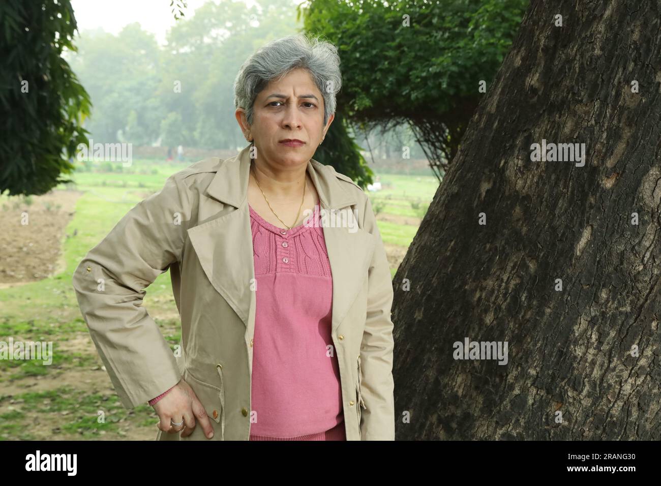 Portrait de femme aux cheveux gris d'âge moyen debout sous l'arbre dans le parc entouré d'un environnement serein et d'air pur. Banque D'Images