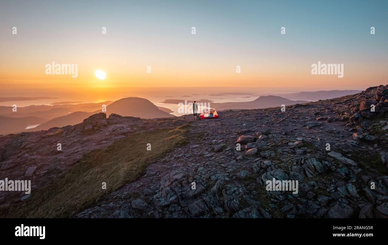 Randonneur profite du coucher du soleil tout en campant au sommet d'un Teallach, témoin de la beauté du paysage des hauts plateaux écossais Banque D'Images