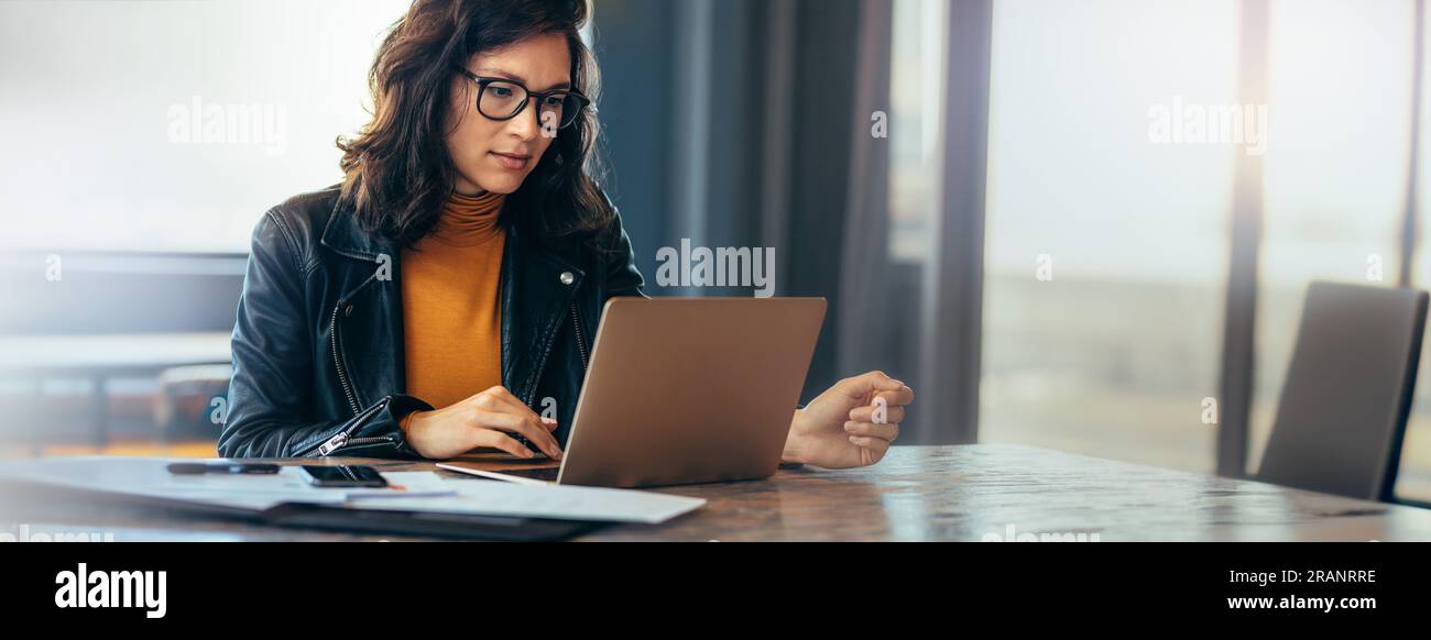 Femme d'affaires asiatique assise à une table dans un bureau, tapant sur son ordinateur portable avec focus. Jeune professionnelle féminine montrant un dévouement et un engagement t Banque D'Images
