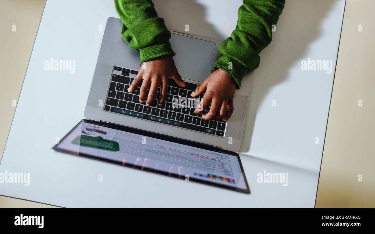 Vue de dessus d'un jeune enfant apprenant à coder avec un ordinateur portable dans une salle de classe. Étudiant noir tapant loin alors qu'il est assis à son bureau complétant un exe de programmation Banque D'Images