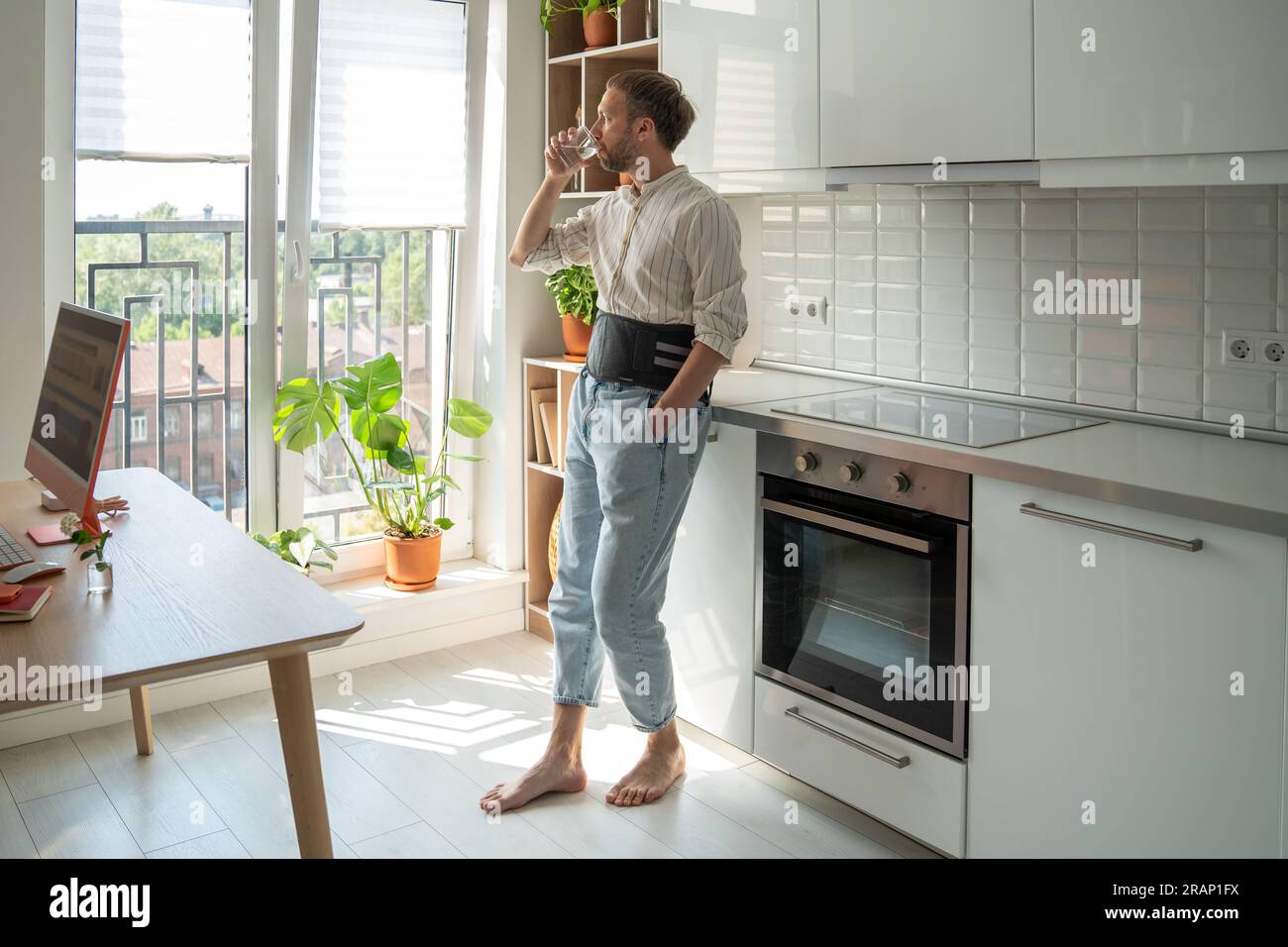 Homme en corset de soutien dorsal sur le bas du dos au traitement d'une hernie sur l'eau potable de cuisine. Banque D'Images