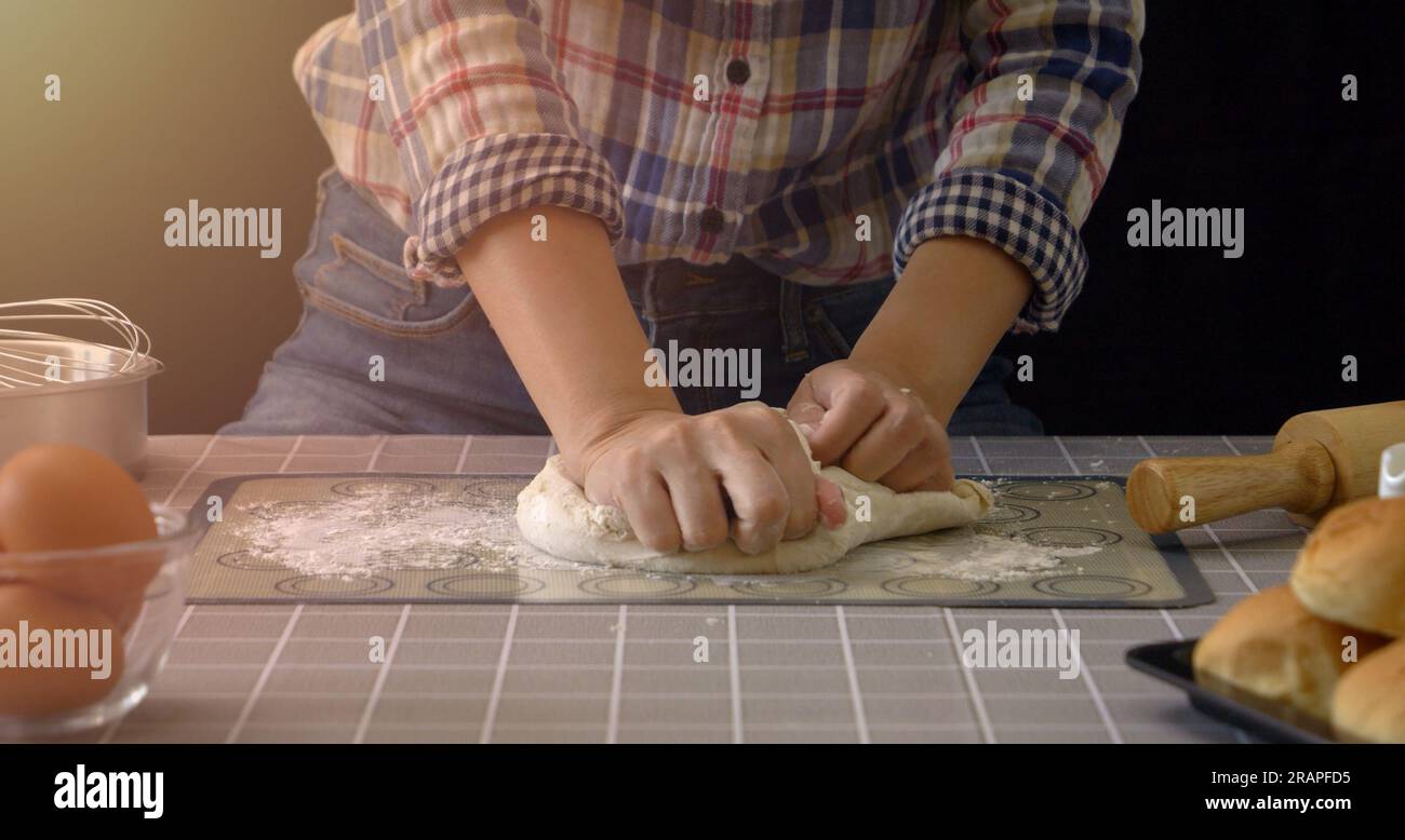 Pain artisanal travaillant avec de la pâte. Pétrissage à la main du pain dans la cuisine avec des outils d'équipement de boulangerie au premier plan et fond noir. Panification Banque D'Images
