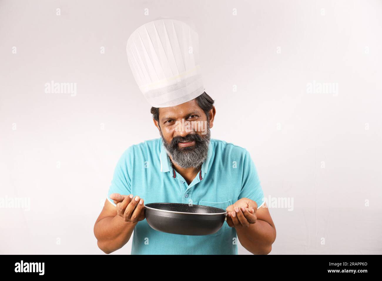 Portrait d'un chef barbu indien portant un t-shirt et une casquette de chef. Heureux souriant expressions fond blanc. Tenir la spatule et la cuillère à frire dans la main Banque D'Images